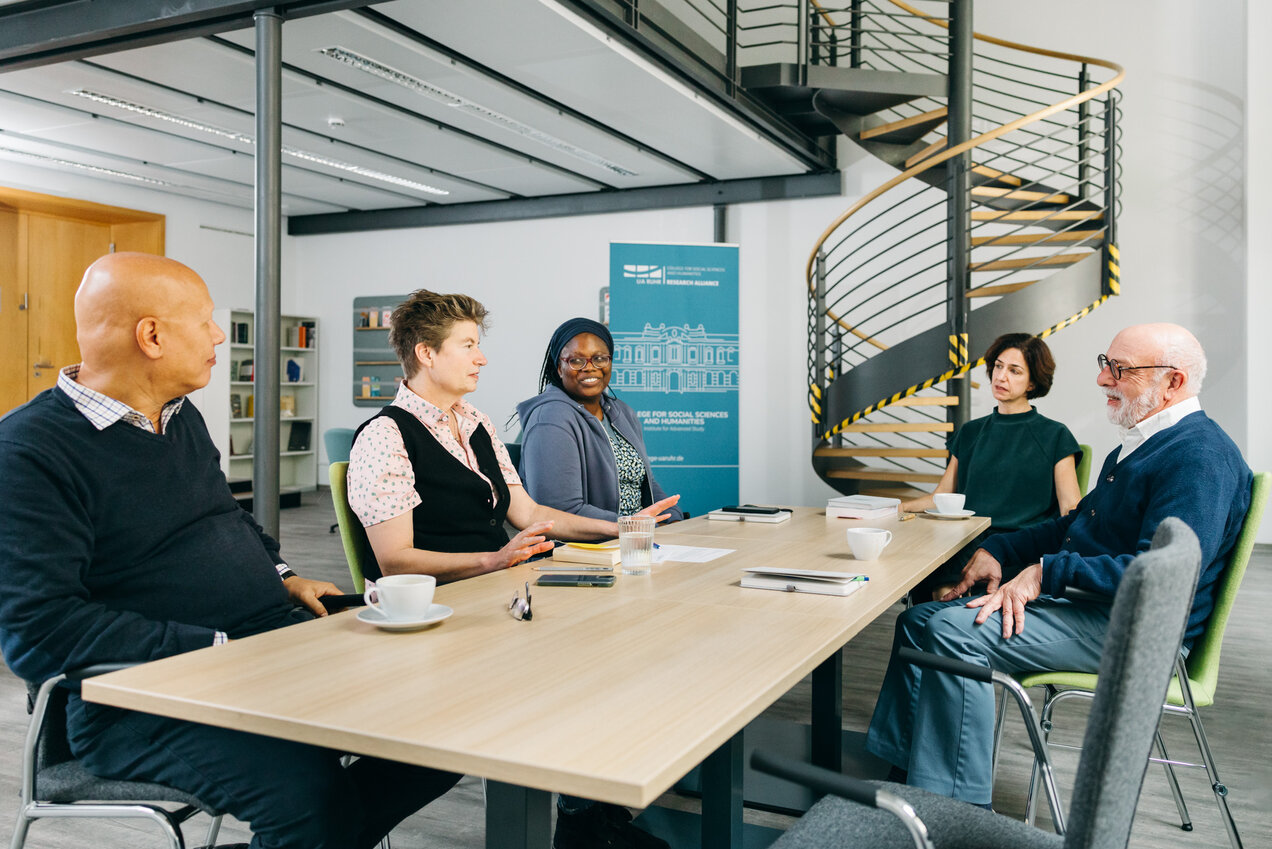 five persons sitting around a table, discussing