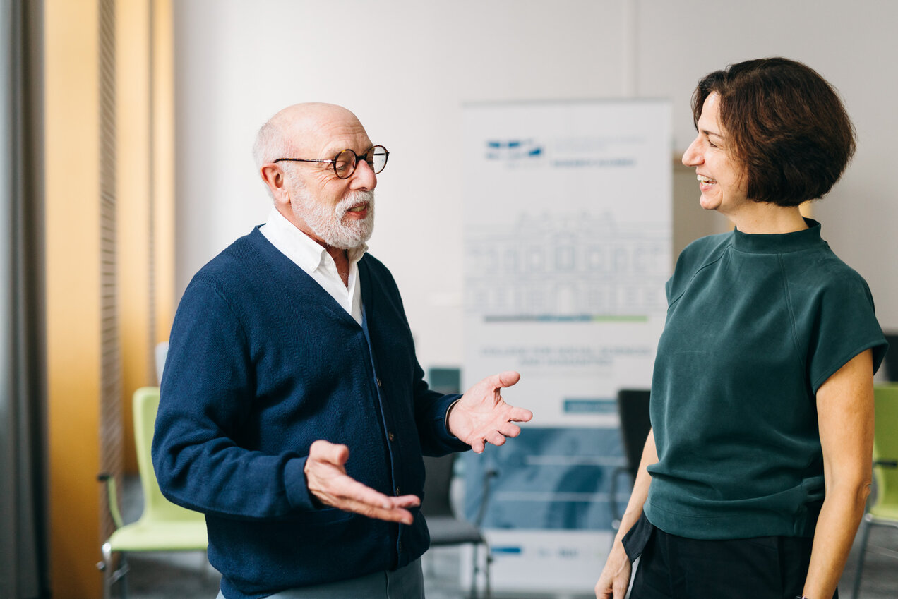 two persons standing beside each other, talking and gesturing